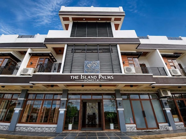 A modern hotel with a prominent logo, large windows, and air conditioning units.