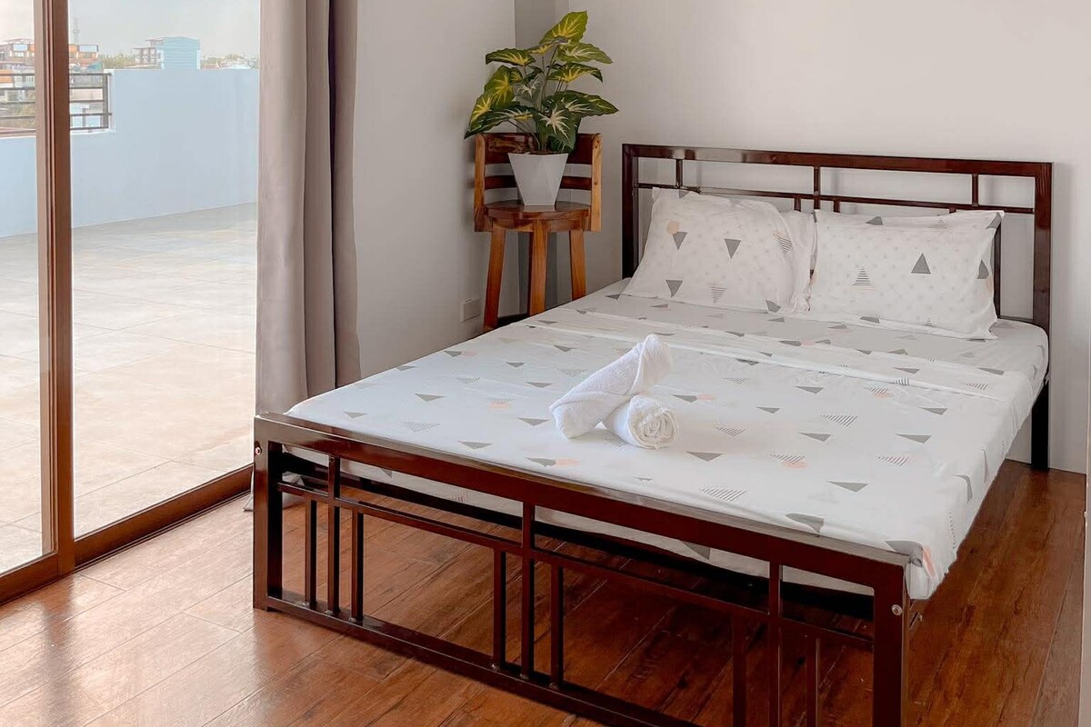 A bedroom with a bed, a potted plant, and a view through a large window.