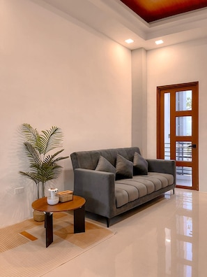 A modern living room with a grey sofa, a small round table, and a potted plant. - The Island Palms Homestay (Alaminos City)