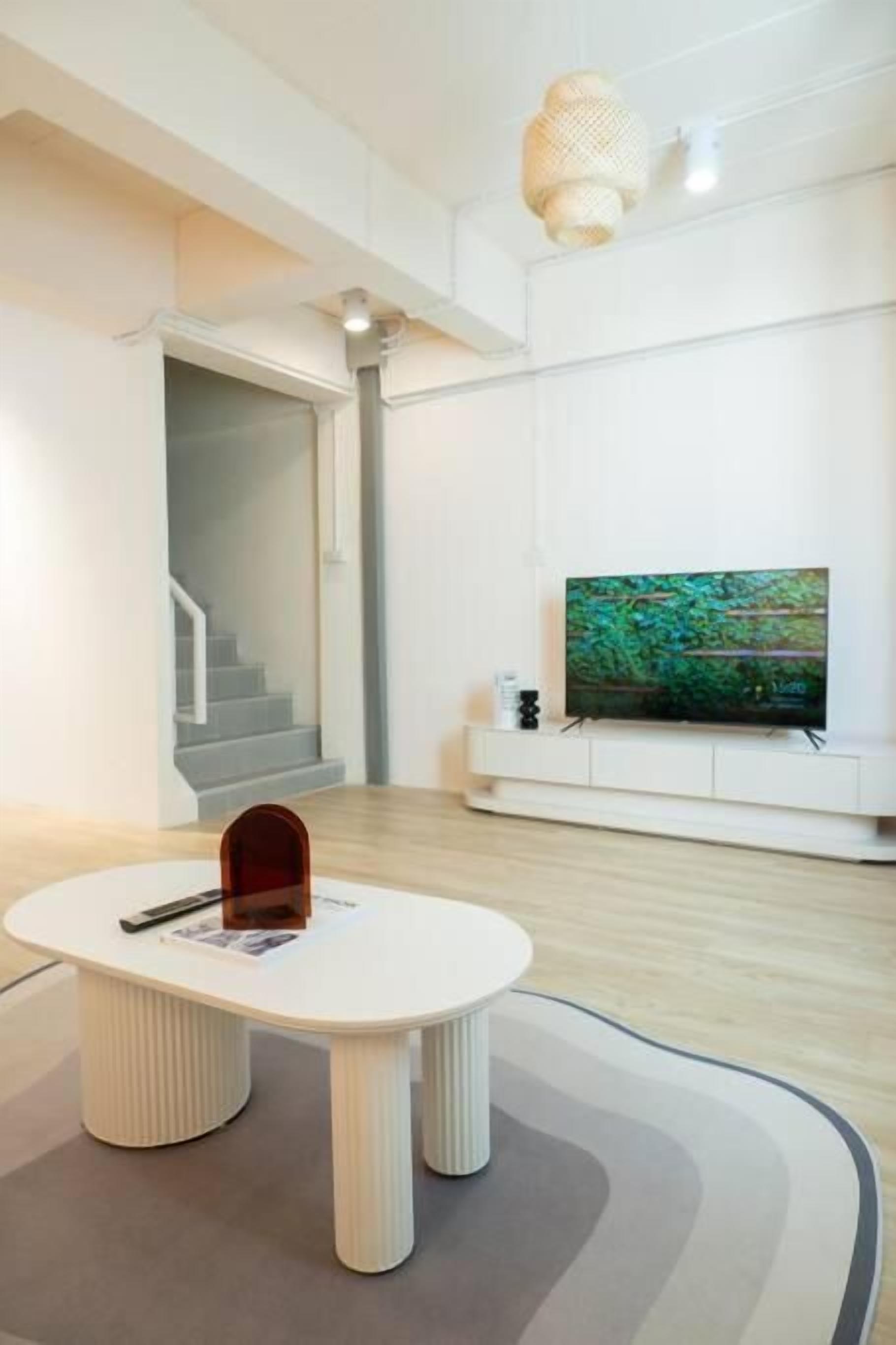 A modern living room with a white sofa, a round coffee table, and a flat-screen TV mounted on the wall.