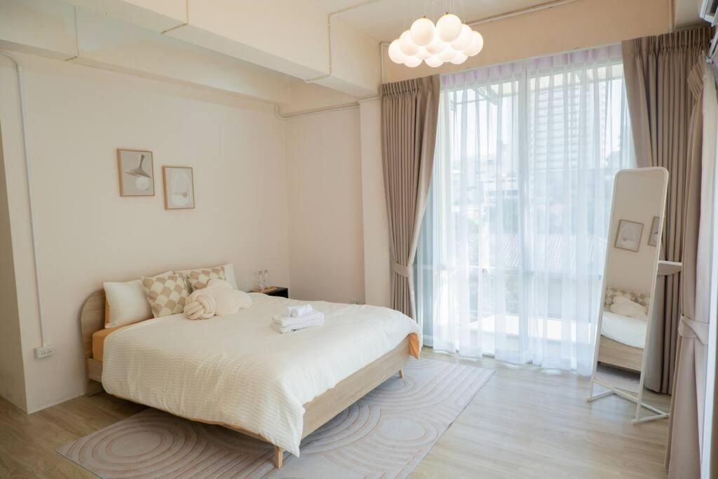 Habitación de hotel moderna con una cama grande, una mesita de noche, una silla y vistas al exterior a través de cortinas translúcidas.