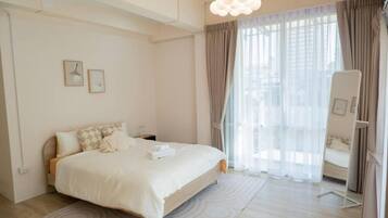 Habitación de hotel moderna con una cama grande, una mesita de noche, una silla y vistas al exterior a través de cortinas translúcidas.