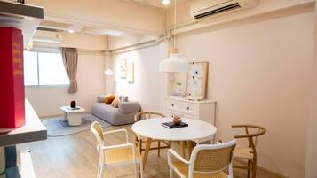 Una habitación de hotel moderna con una mesa redonda, sillas blancas, un sofá y una mesita auxiliar.