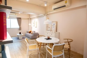 Una habitación de hotel moderna con una mesa redonda, sillas blancas, un sofá y una mesita auxiliar.