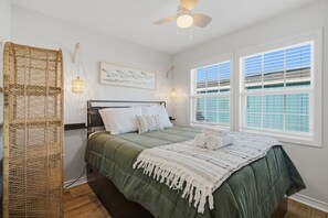 Ein Schlafzimmer mit einem Bett, einem gewebten Korb, einem Deckenventilator und einem Fenster mit Jalousien.