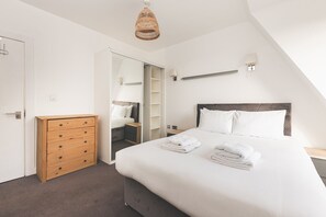 A bedroom with a bed, a wooden dresser, a wardrobe, and a hanging light fixture. - Bethnal Green Penthouse & Terrace (London)