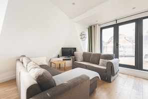 A modern living room with a sofa, a coffee table, and a flat-screen TV. - Bethnal Green Penthouse & Terrace (London)