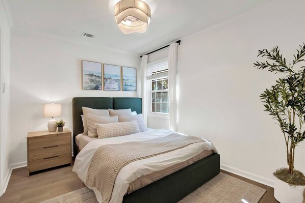 Un dormitorio con cama, mesita de noche, lámpara y una planta en maceta.