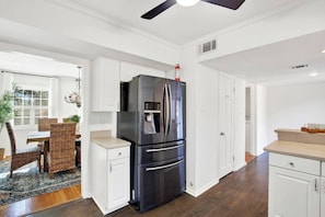 Una cocina moderna con armarios blancos, un refrigerador de acero inoxidable y una zona de comedor con sillas de mimbre.
