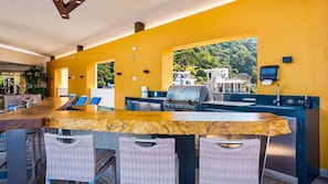 A bar area with a marble countertop, wicker chairs, and a view of a forested area.
