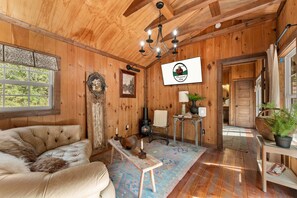 A cozy cabin interior with a wooden ceiling, a sofa, a fireplace, and a dining area. - Creek Mornings, Fire-Pit Nights • Cozy Cottage Near Thunder Ridge (Blue Eye)