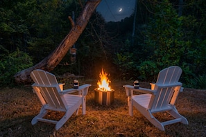 Two Adirondack chairs facing a campfire with a lantern and a can on the table. - Creek Mornings, Fire-Pit Nights • Cozy Cottage Near Thunder Ridge (Blue Eye)