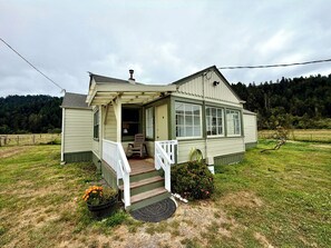 Une maison de plain-pied avec un porche, une porte d’entrée et un petit jardin agrémenté de fleurs.