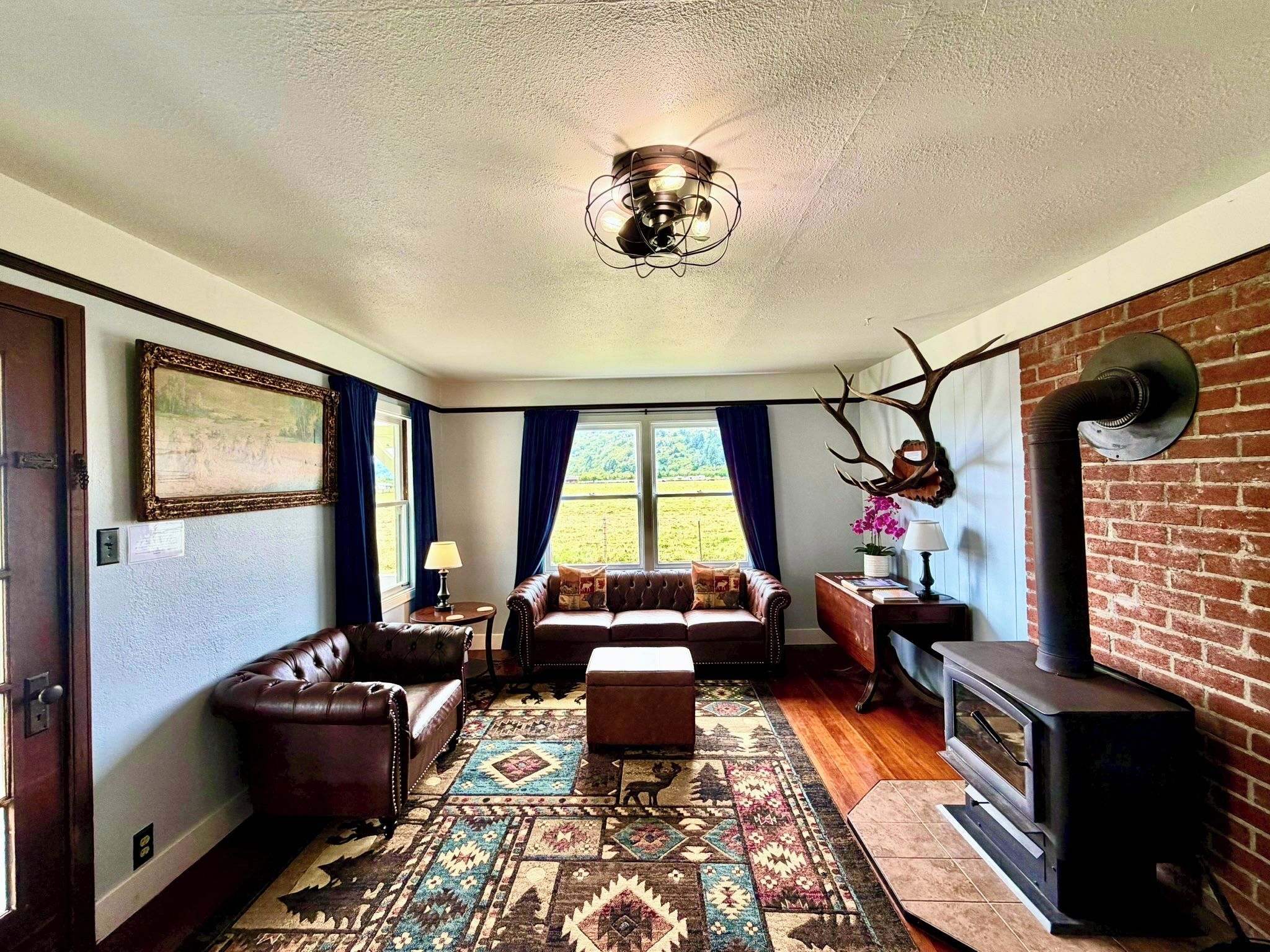 Una sala de estar con chimenea, sofá de cuero, alfombra estampada y un ventanal con cortinas.