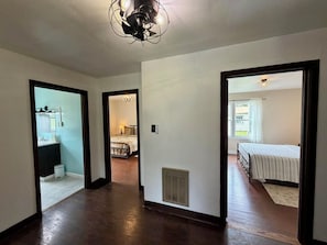 A hallway leading to a bedroom with a bed, a bathroom with a sink, and a kitchen area. - Redwood Valley Farmhouse | Ranch Stay + Game Room (Orick)