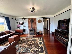 A living room with a fireplace, a sofa, a rug, and a television. - Redwood Valley Farmhouse | Ranch Stay + Game Room (Orick)