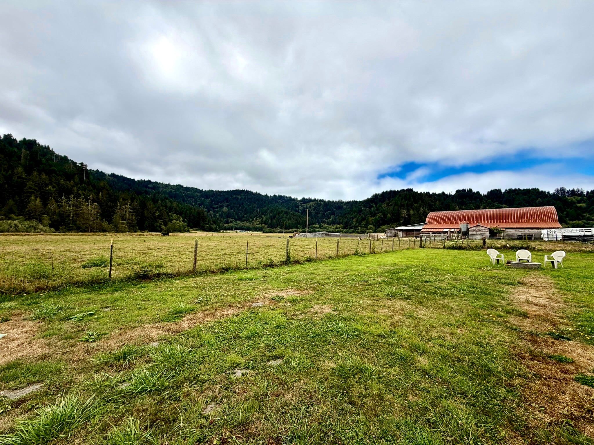 A rural landscape with a fenced field, a red barn, and a forested hill in the background.
