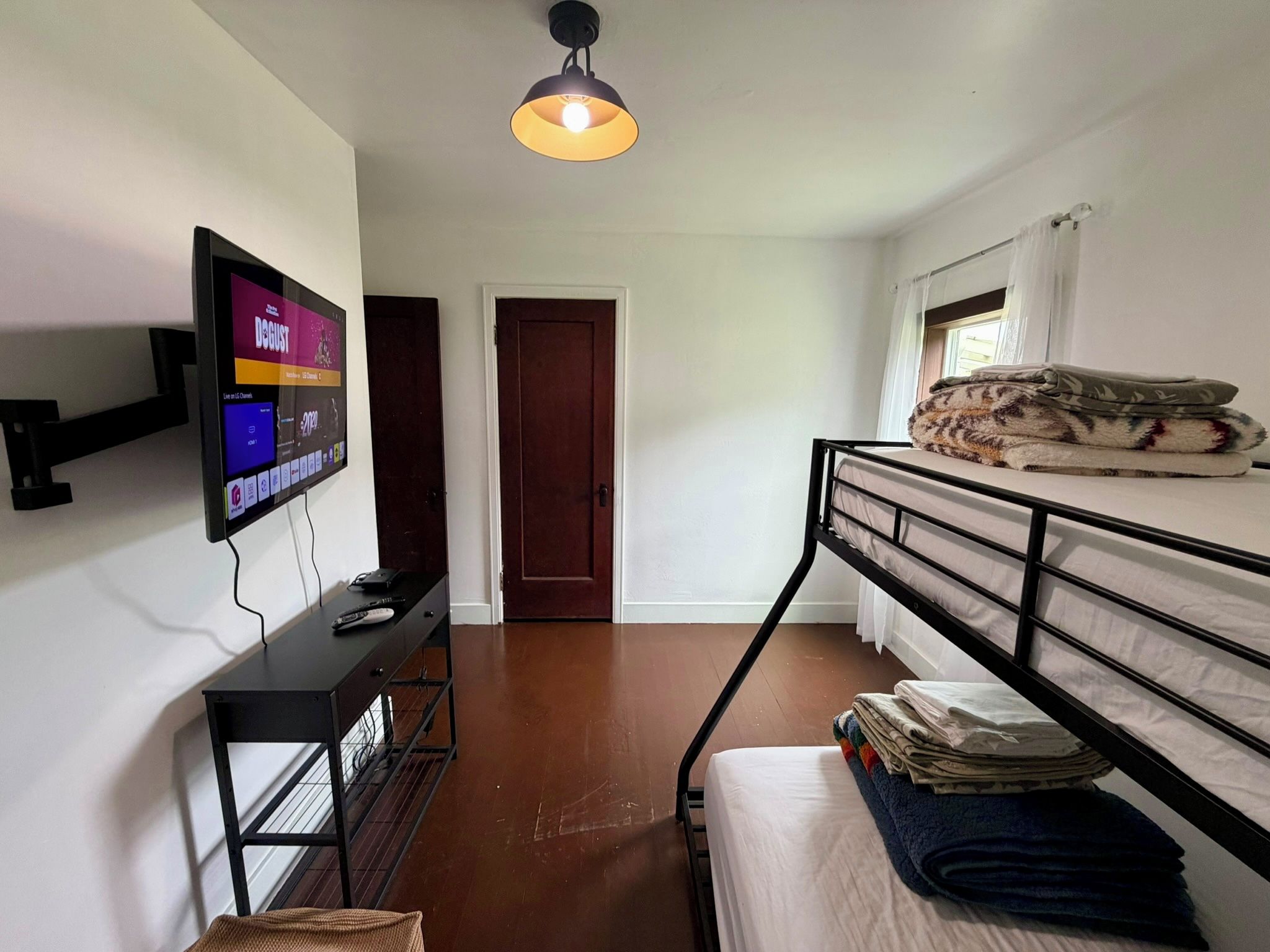 Una habitación compacta con una cama individual alta, un escritorio con televisor de pantalla plana, una mesita pequeña y una lámpara colgante.