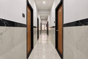 Un pasillo con suelo de mármol, puertas de madera y un extintor en la pared.