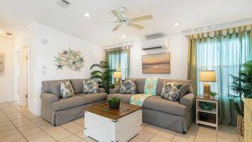 A living room with a sectional sofa, a coffee table, a ceiling fan, and a painting on the wall.