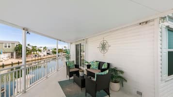 A balcony with a view of a marina, a dining table with chairs, and a decorative wall piece.
