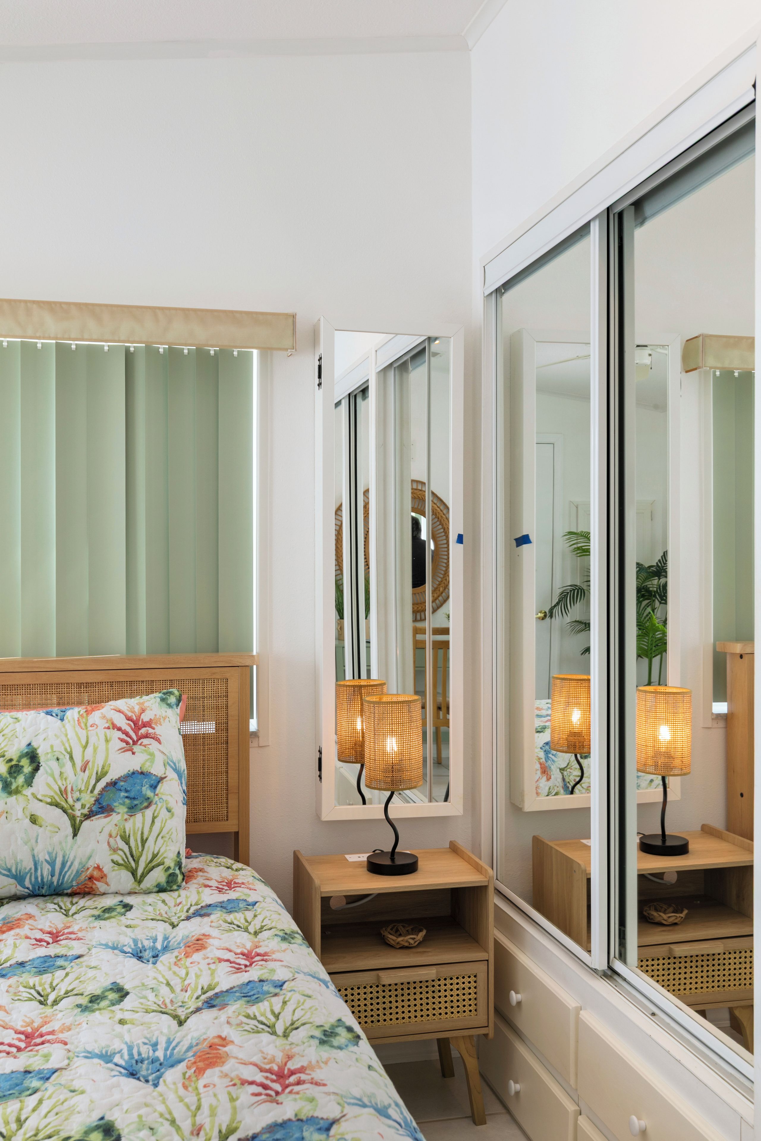 A hotel room with a bed, bedside lamps, a mirror, and a window with blinds.