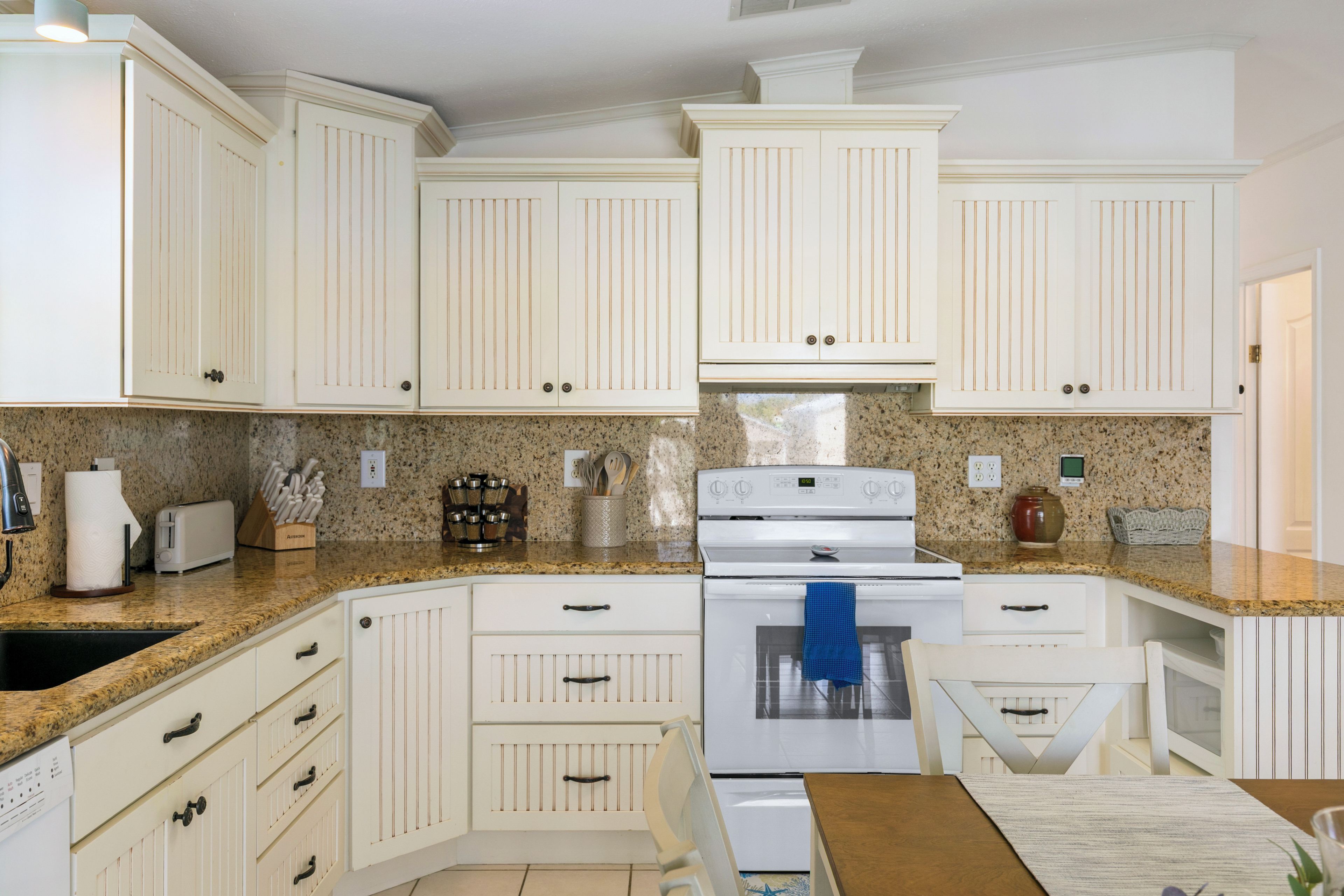 A kitchen with white cabinetry, a granite countertop, a stove, and a sink.