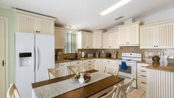 A kitchen with white cabinetry, a dining table with chairs, a refrigerator, and a stove.