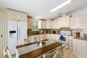 A kitchen with white cabinetry, a dining table with chairs, a refrigerator, and a stove. - Florida Keys Waterfront Escape - 2BR with 44' Seawall (Cudjoe Key)