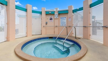 A hot tub with a tiled edge, surrounded by beige walls and white lattice panels.