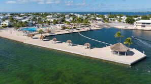 A coastal resort with a swimming pool, beach umbrellas, and a marina. - Florida Keys Waterfront Escape - 2BR with 44' Seawall (Cudjoe Key)