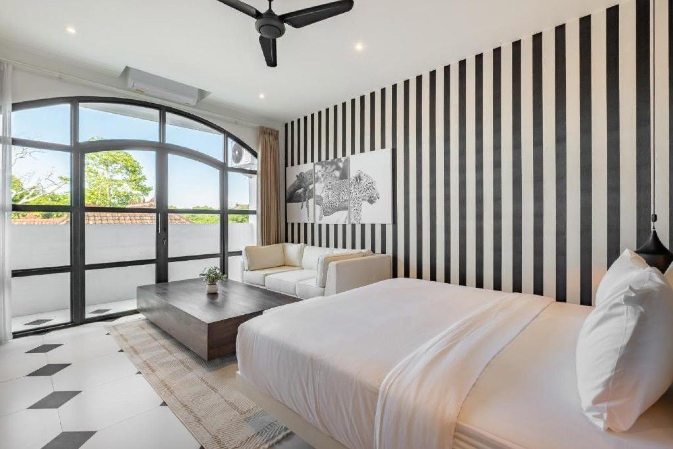 Une chambre moderne avec un grand lit, un canapé, une table basse et une vue dégagée sur l’extérieur grâce à une grande fenêtre.