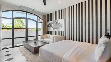 Une chambre moderne avec un grand lit, un canapé, une table basse et une vue dégagée sur l’extérieur grâce à une grande fenêtre.