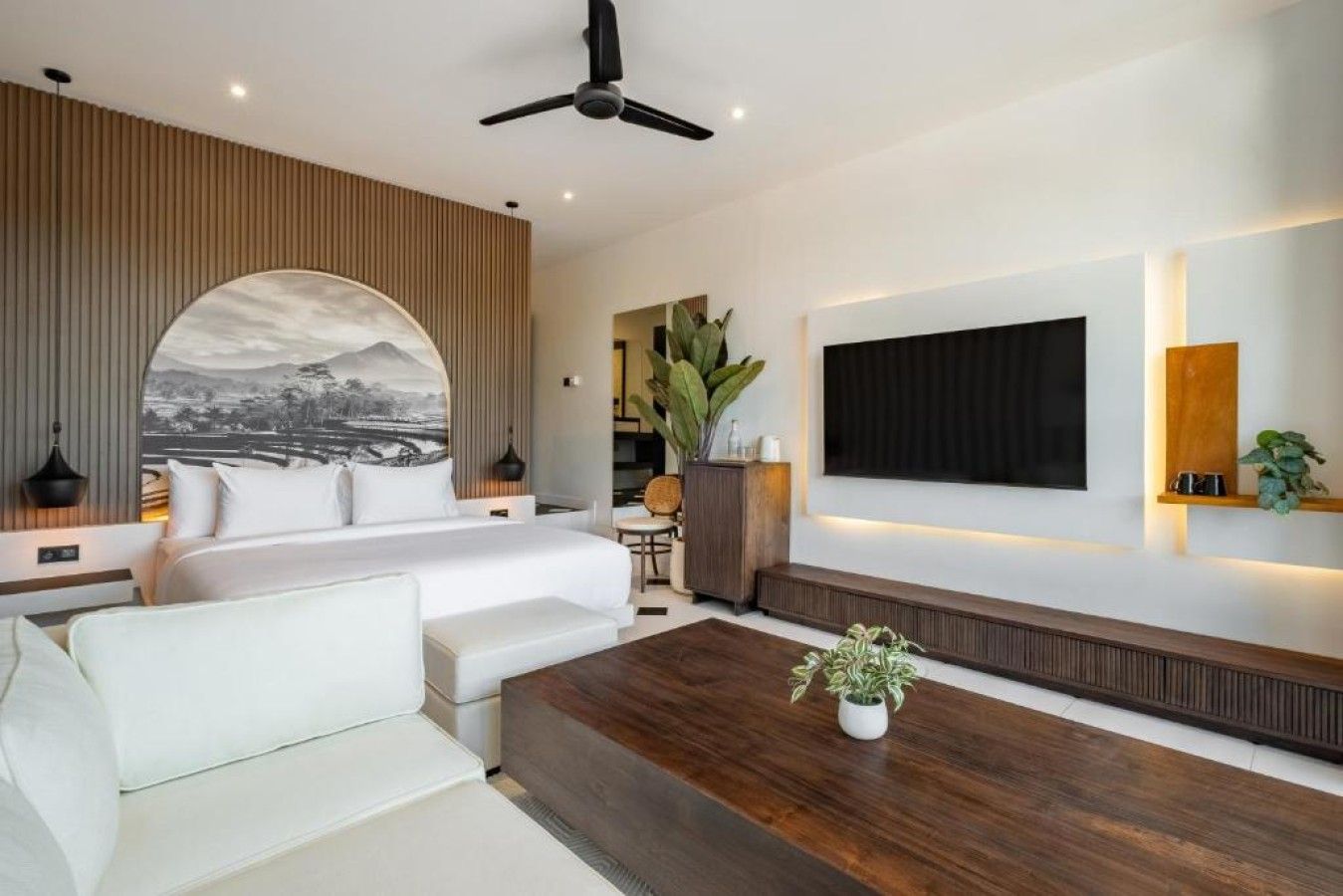 Une chambre d’hôtel moderne équipée d’un lit, d’un coin salon, d’une grande télévision et d’un ventilateur de plafond.