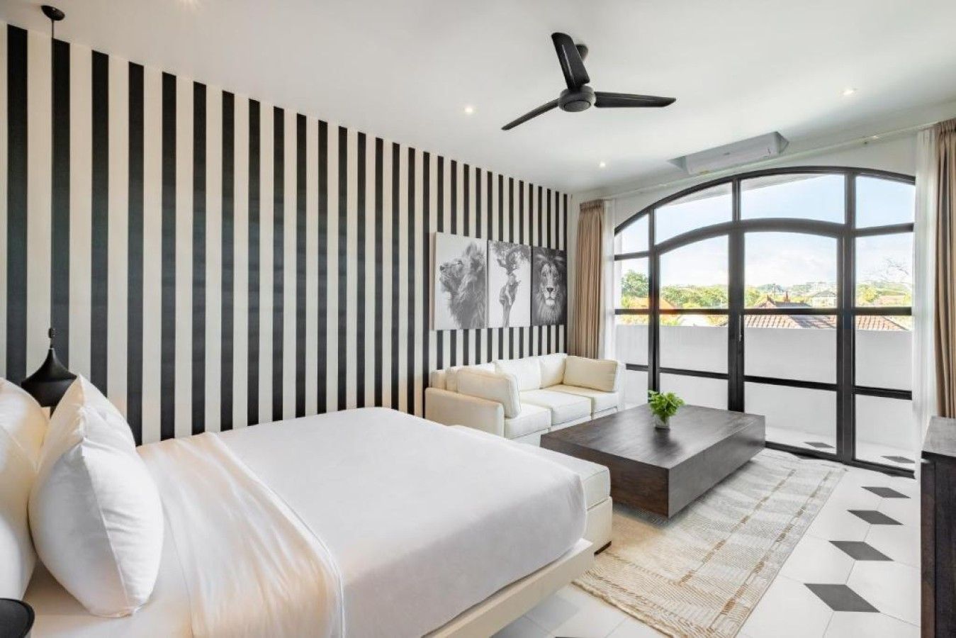 A modern bedroom with a large bed, a sofa, a coffee table, and a ceiling fan.