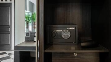 A secure safe with a digital keypad, placed on a wooden cabinet in a room with a checkered floor and a view of a balcony with plants.