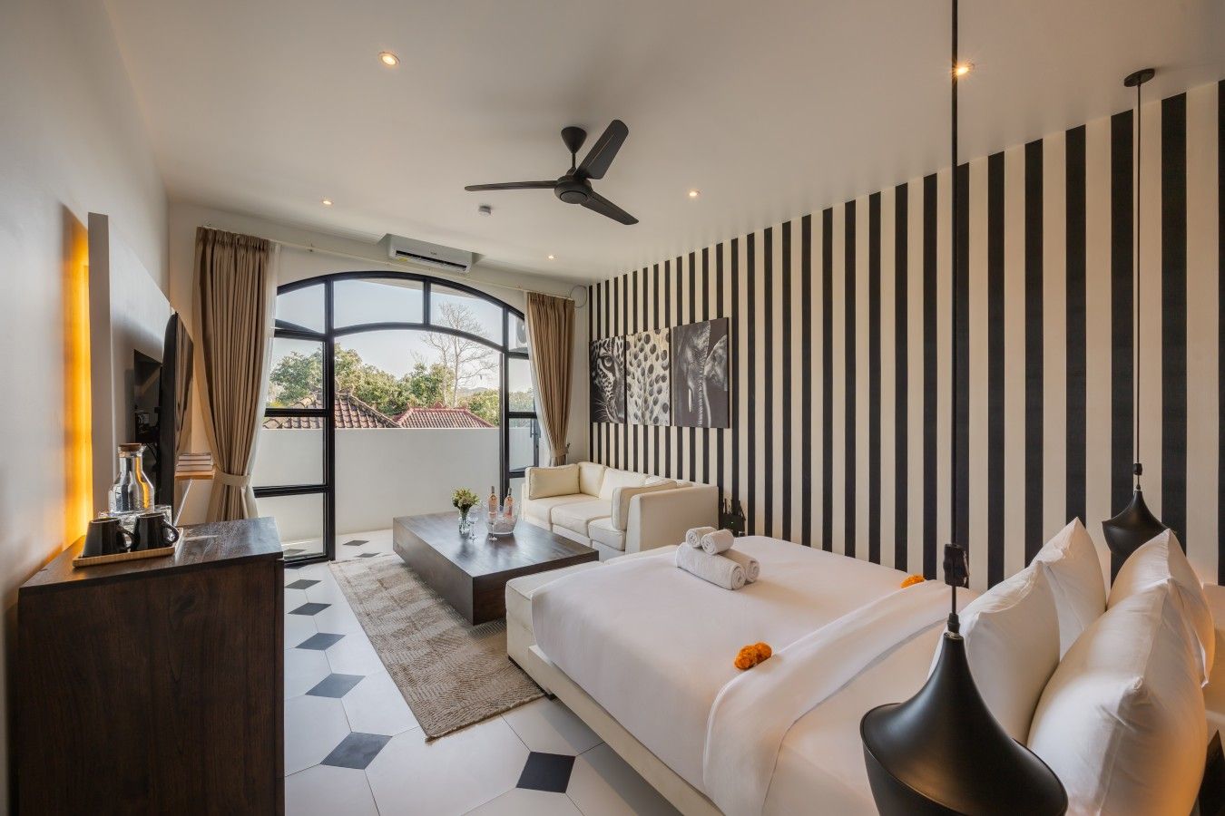 A modern hotel room with a large bed, a seating area, and a view through a glass door.