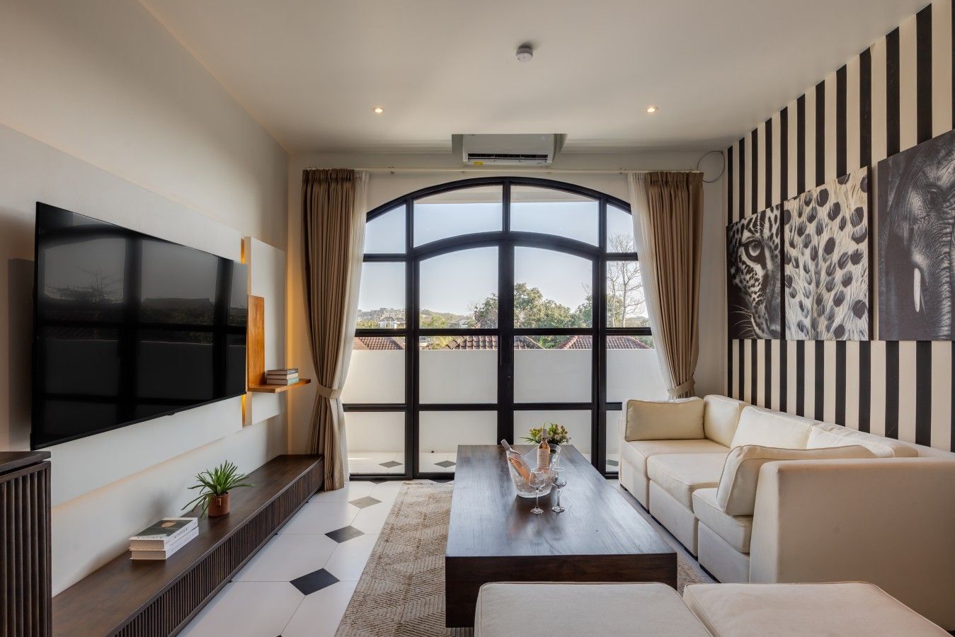 A modern living room with a flat-screen TV, a sofa, a coffee table, and a large window with curtains.