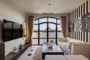A modern living room with a flat-screen TV, a sofa, a coffee table, and a large window with curtains. - 2 BR Apartement Near Thomas Beach, Uluwatu (South Kuta)