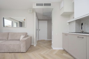 Un espacio habitable moderno y minimalista con un sofá, una zona de cocina y un pasillo que conduce a otra habitación.