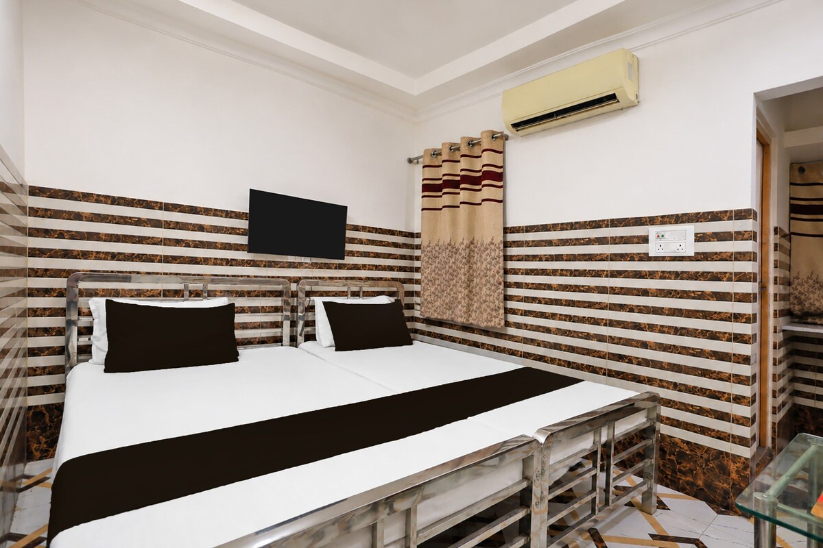 A hotel room with a bed, a flat-screen TV, an air conditioning unit, and a patterned curtain.