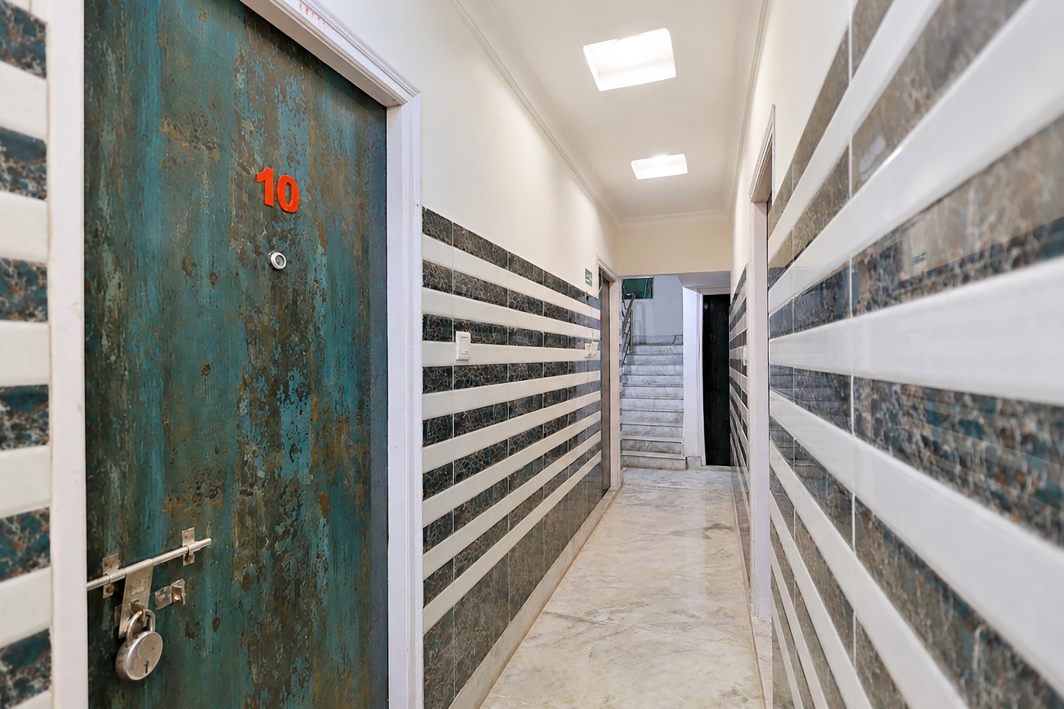 A hallway with a metal door, white railings, and a tiled floor.