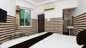 A bedroom with a bed, a window with curtains, an air conditioning unit, and a bathroom with a sink.