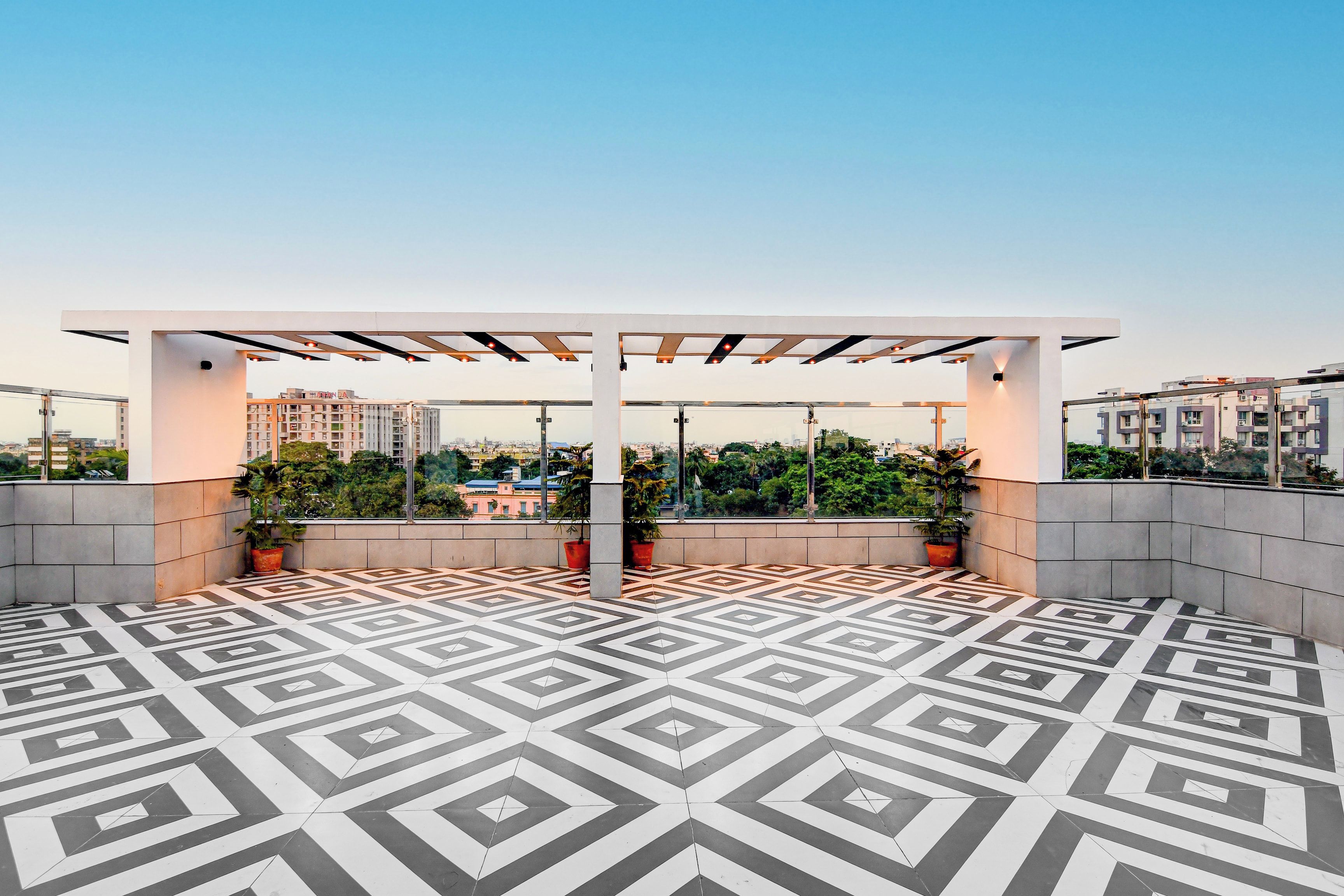 Terraço no telhado com piso de padrão geométrico, plantas em vasos e estrutura de pérgola.