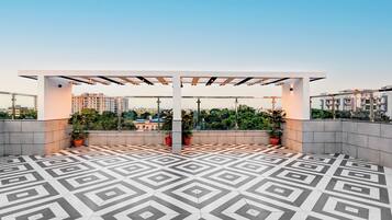 Terraço no telhado com piso de padrão geométrico, plantas em vasos e estrutura de pérgola.