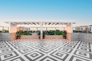 Una terraza en la azotea con suelo de diseño geométrico, plantas en macetas y una estructura de pérgola.