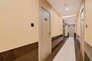 Un pasillo de hotel con puertas numeradas, piso de mármol e iluminación empotrada en el techo.