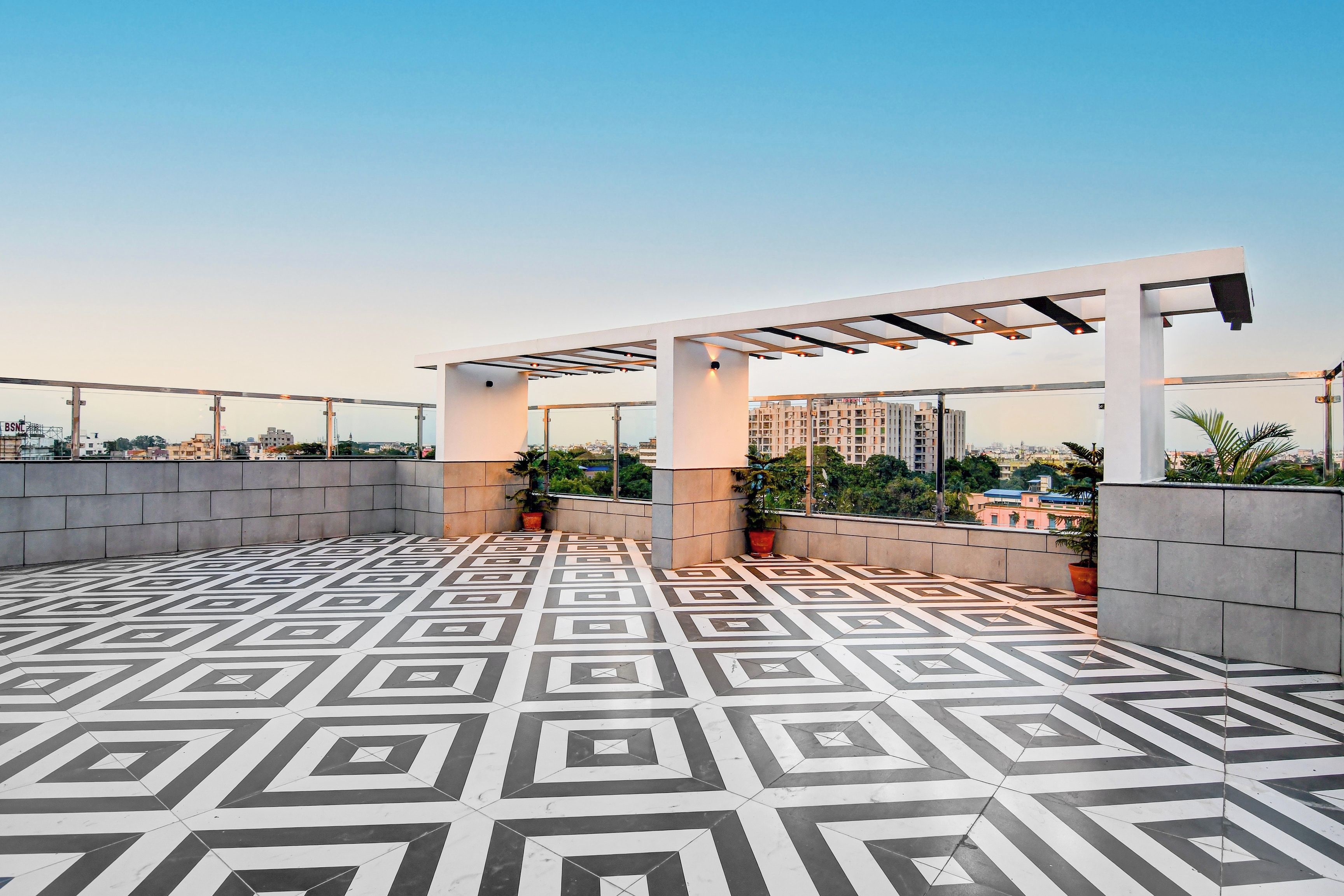 Eine Dachterrasse mit einem geometrischen Bodenmuster, Topfpflanzen und einer Pergola.