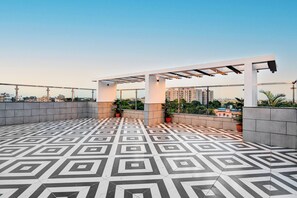 Una terraza en la azotea con suelo de diseño geométrico, plantas en macetas y una estructura de pérgola.
