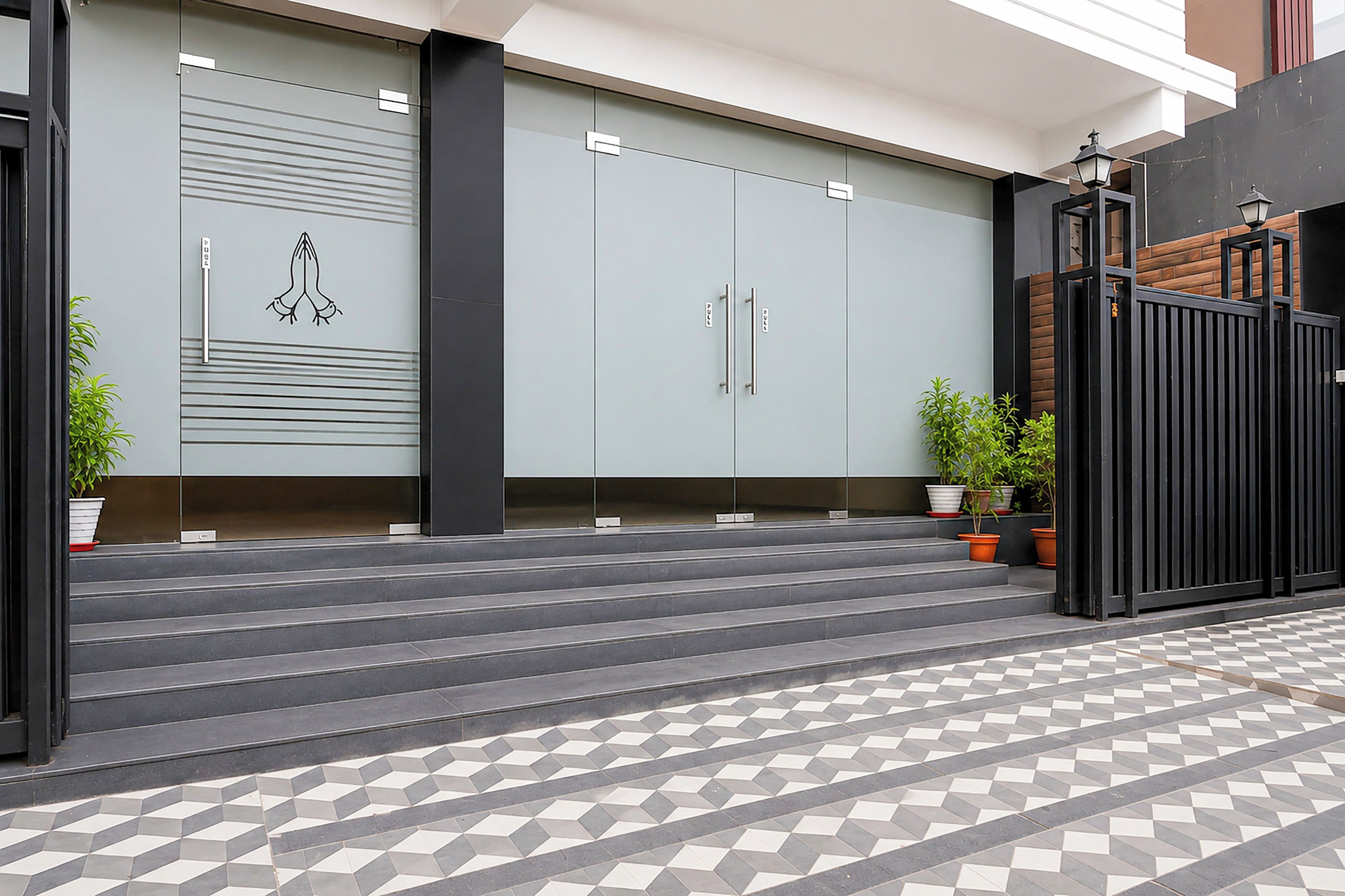 A modern building entrance with a set of steps leading up to a gated area, flanked by potted plants and a patterned tile floor.